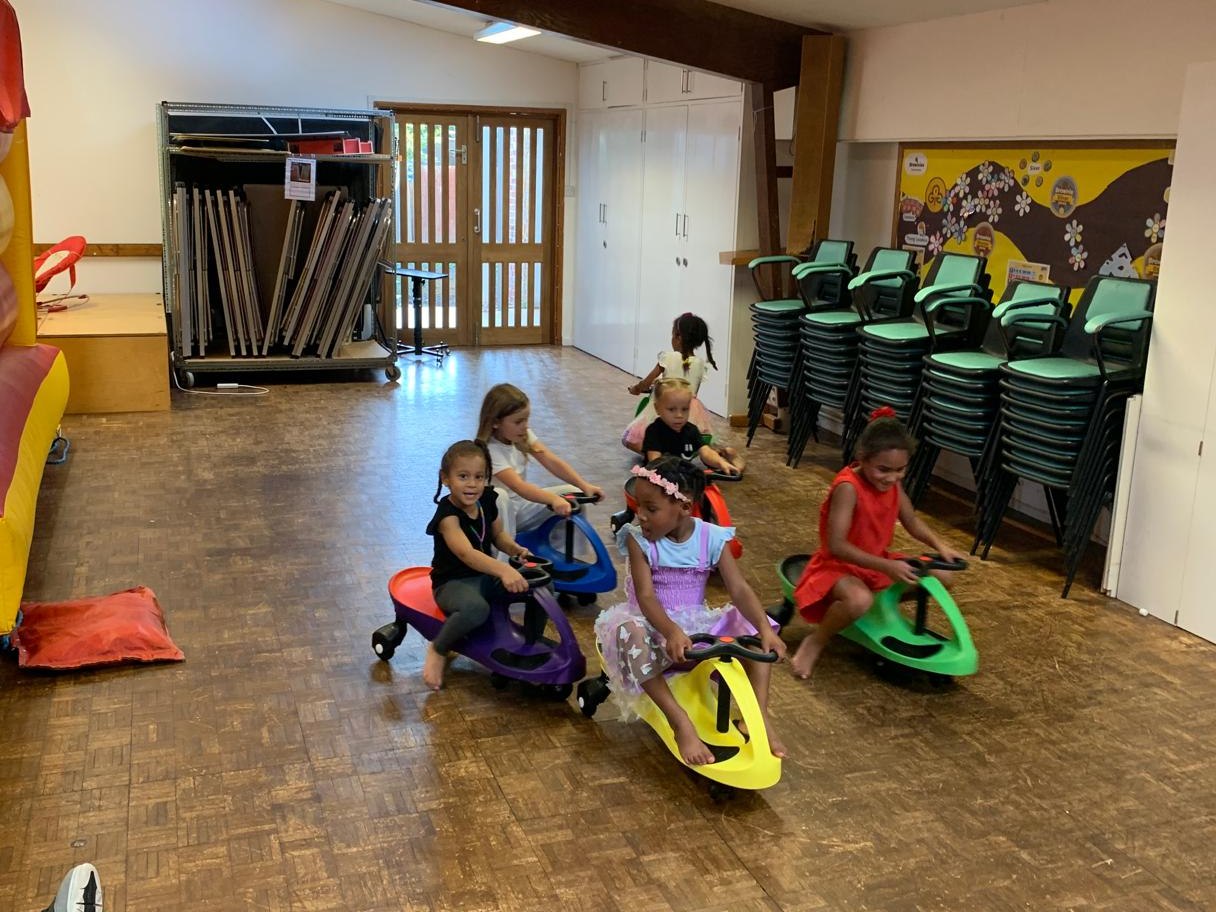 Children riding colourful swing cars in a hall next to a bouncy castle